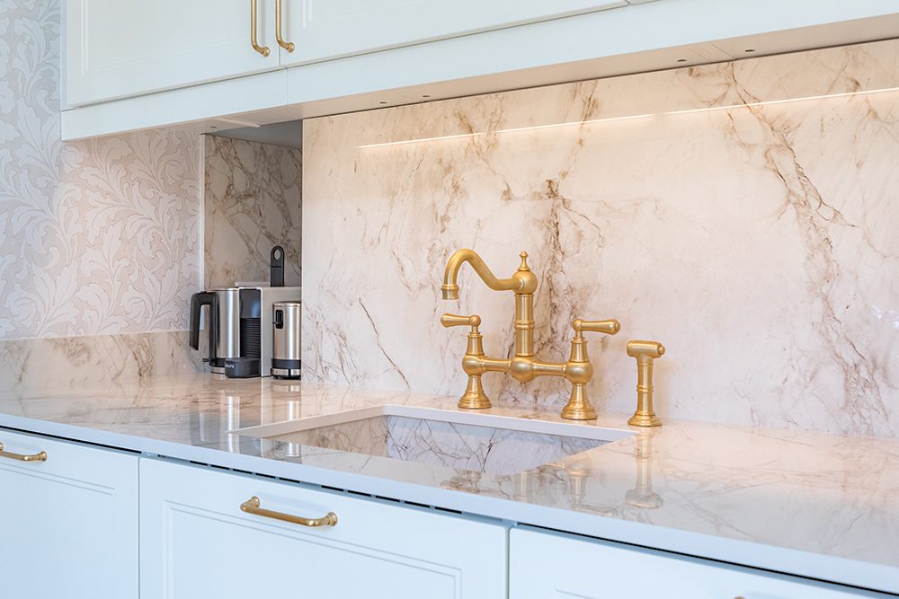 Tour du Pin Paris fractional ownership Bright kitchen with white cabinets, gold faucet, marble backsplash, and counter appliances.